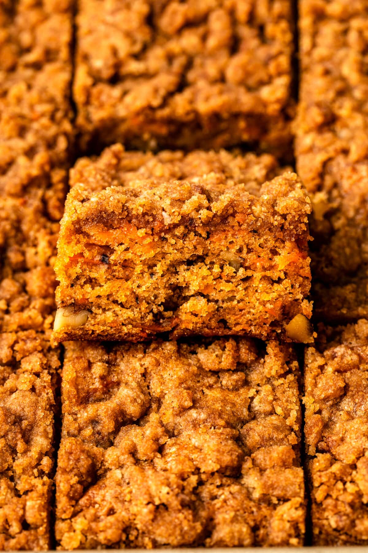 a zoomed in image of a slice of carrot cake coffee cake in a baking tray full of freshly baked slices of cake