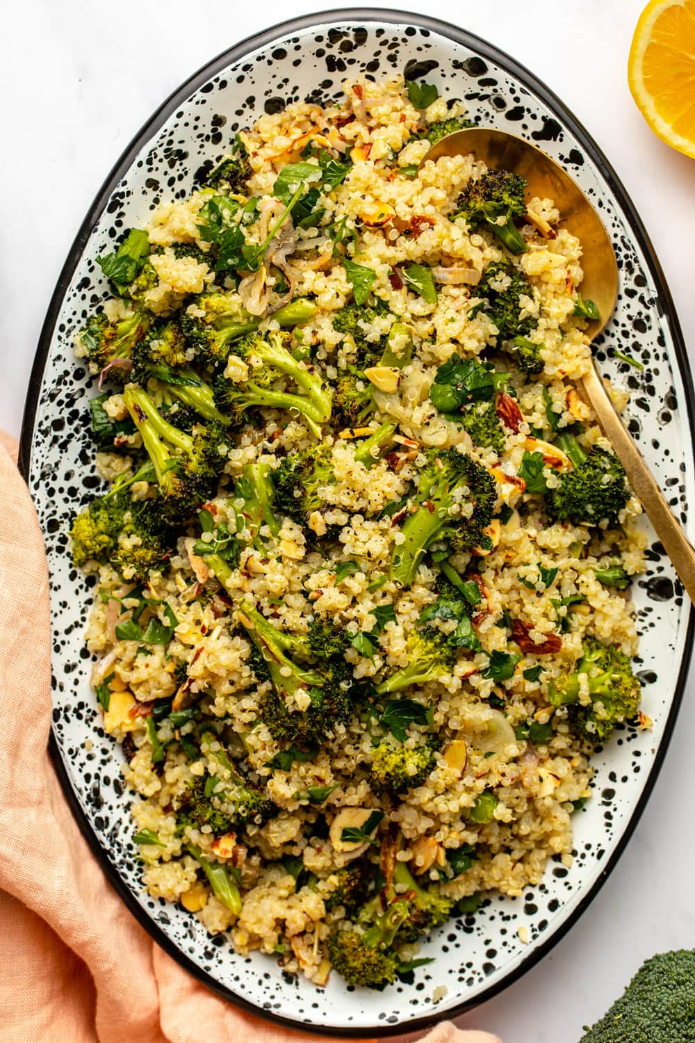 roasted broccoli quinoa salad served on a large oval plate with a serving spoon digged in