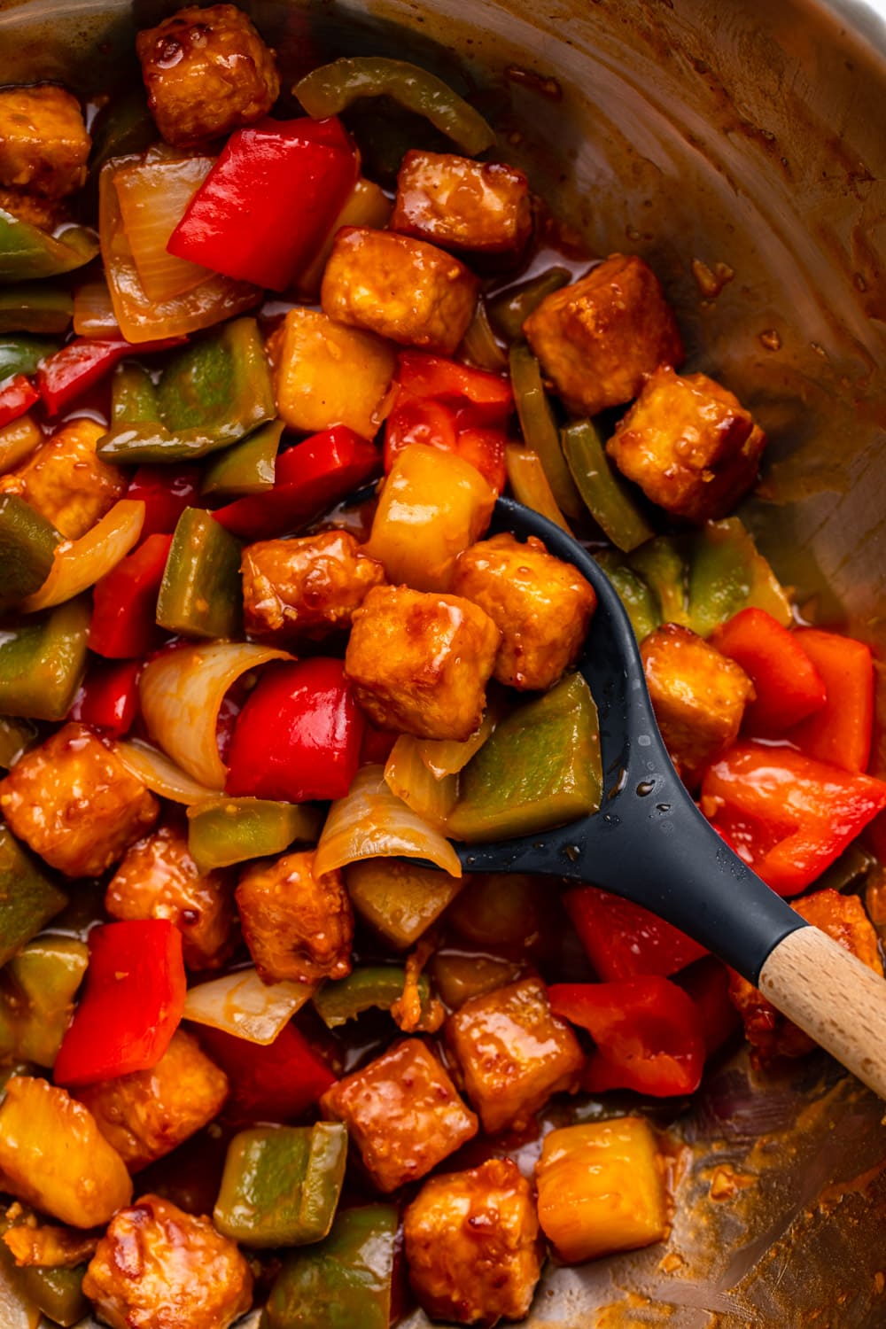 sweet and sour tofu in a pan with a serving spoon giving it a mix