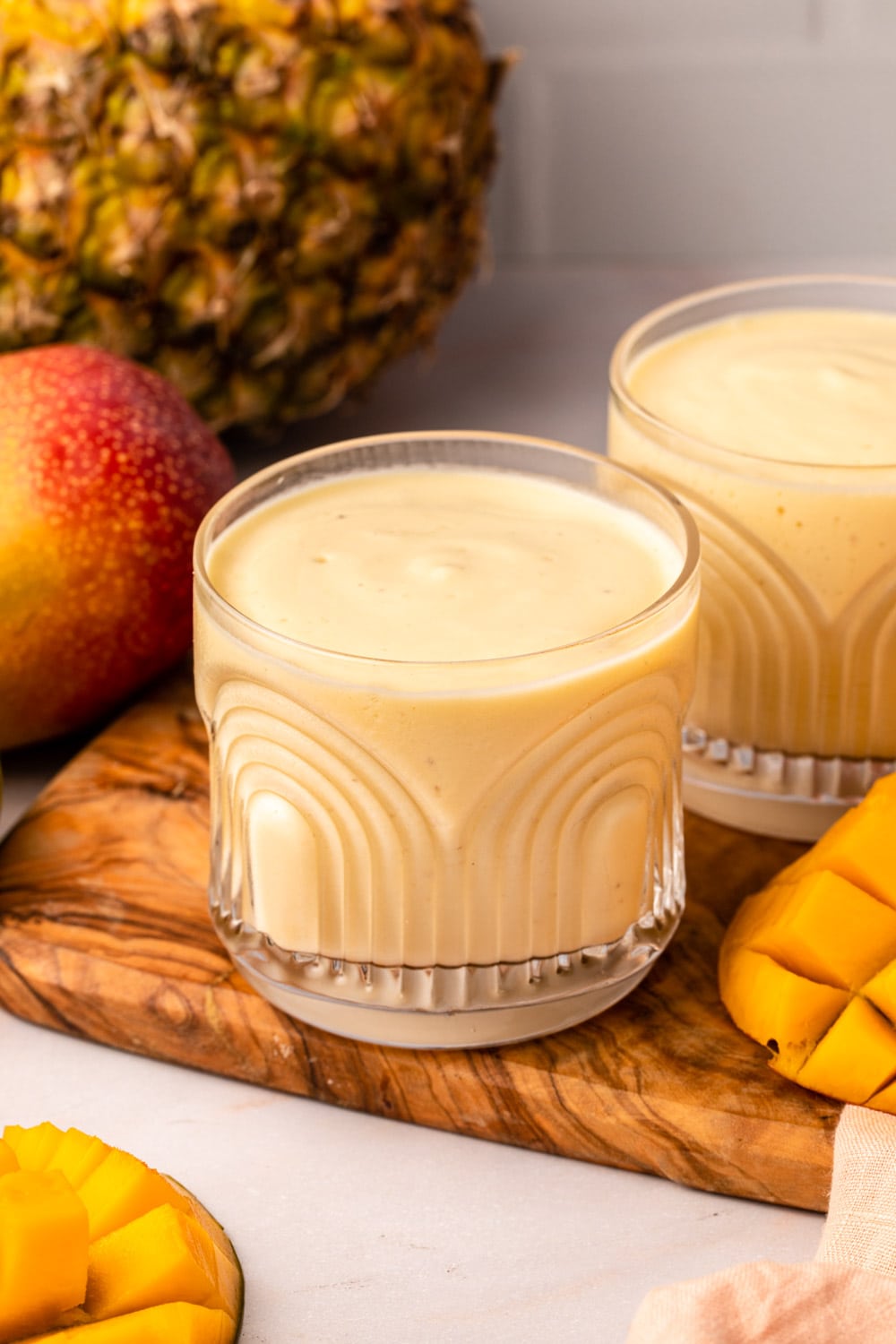 a glass of mango pineapple smoothie on a serving board
