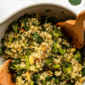 roasted broccoli quinoa salad in a large bowl with two serving spoons stirring