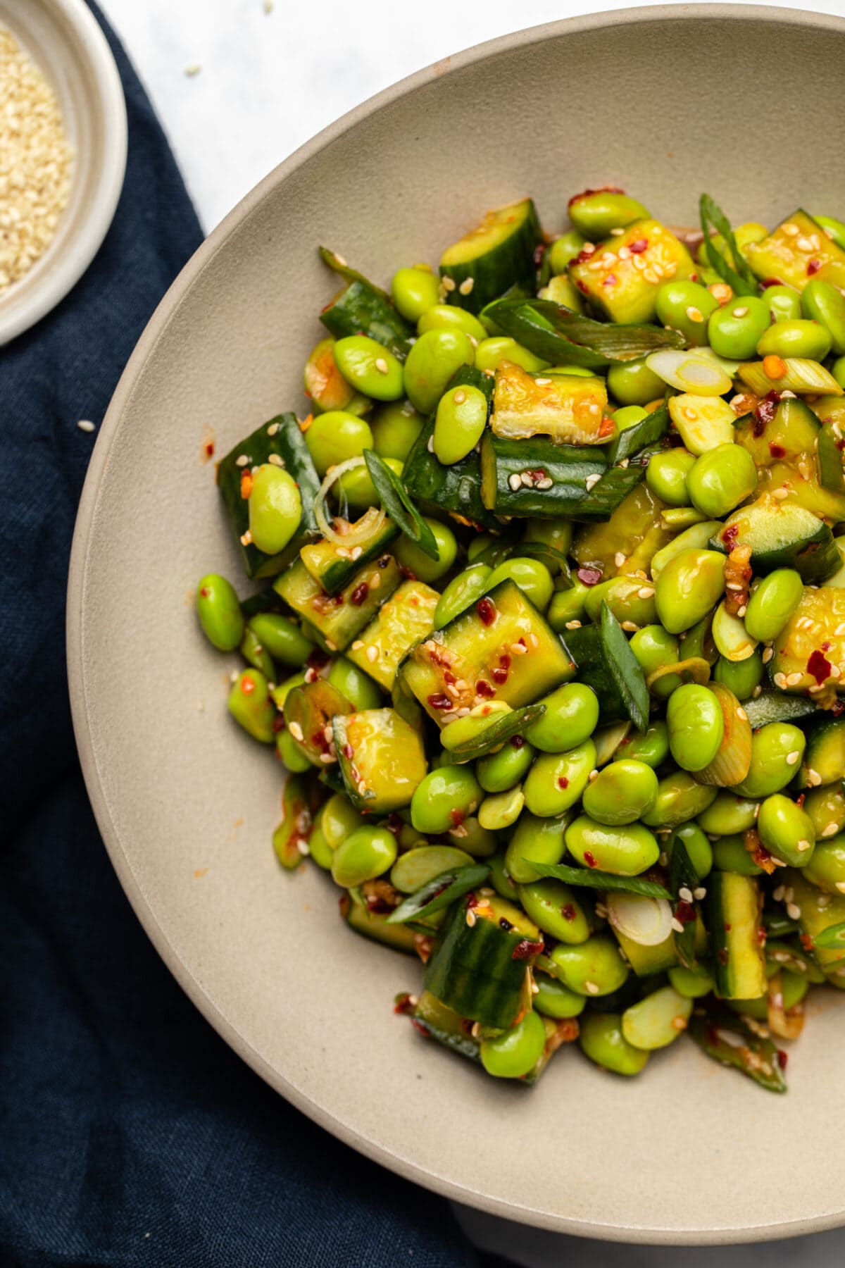 close up photo of edamame salad with smashed cucumbers, sesame seeds, chili oil, and green onions served in a bowl