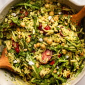 pesto orzo salad in bowl with wooden tongs