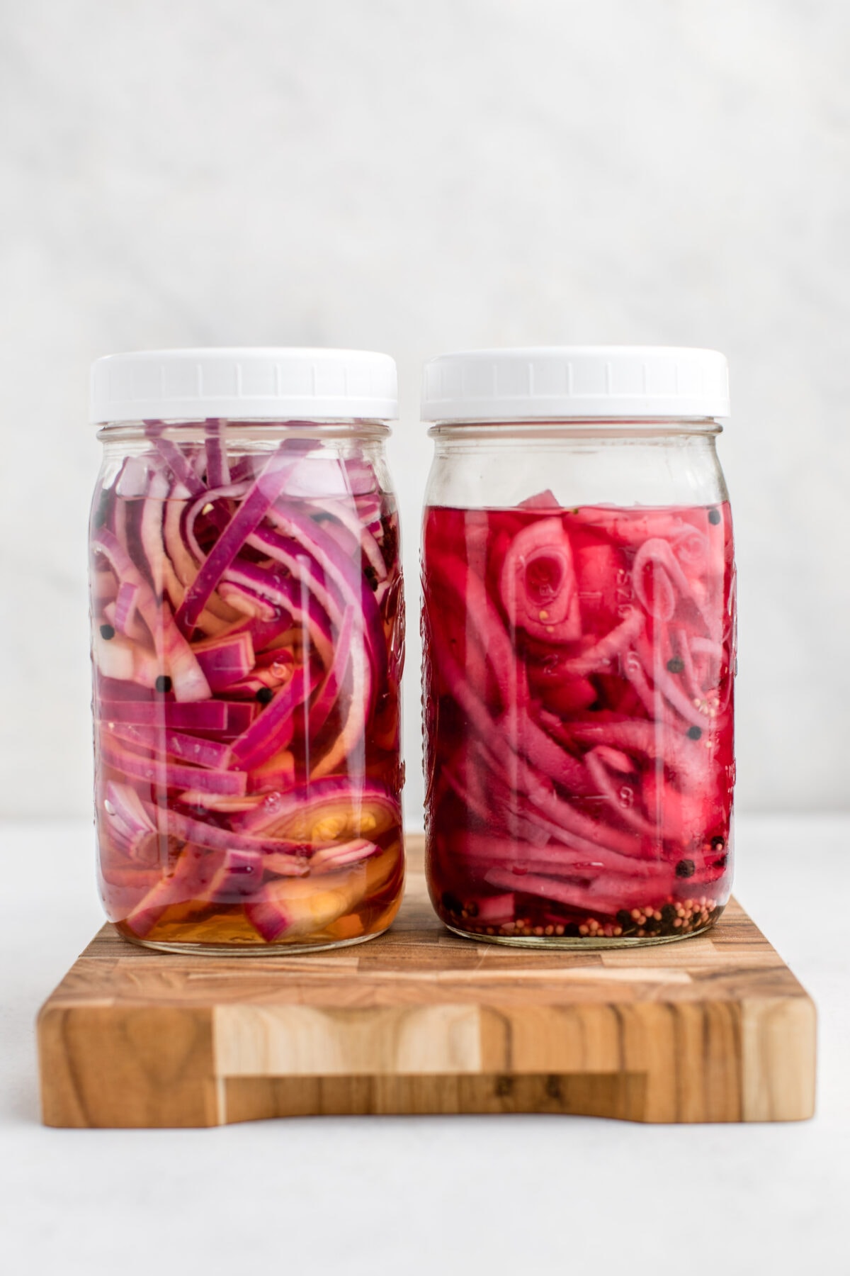 two glass jars of pickled red onions on a cutting board