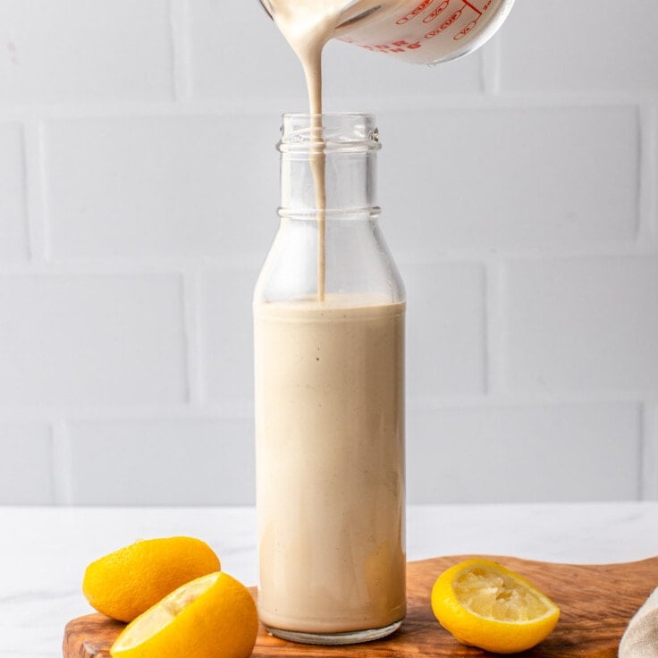 pouring tahini dressing into glass bottle