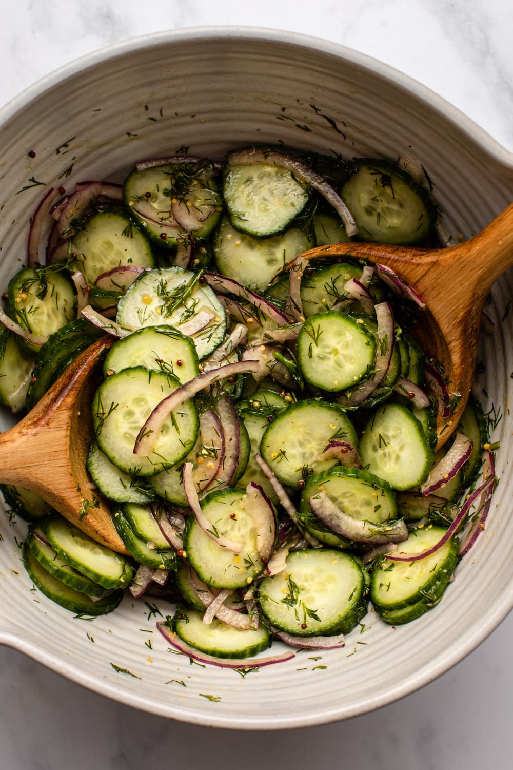 cucumber dill salad in a huge bowl with two wooden spoons stirring