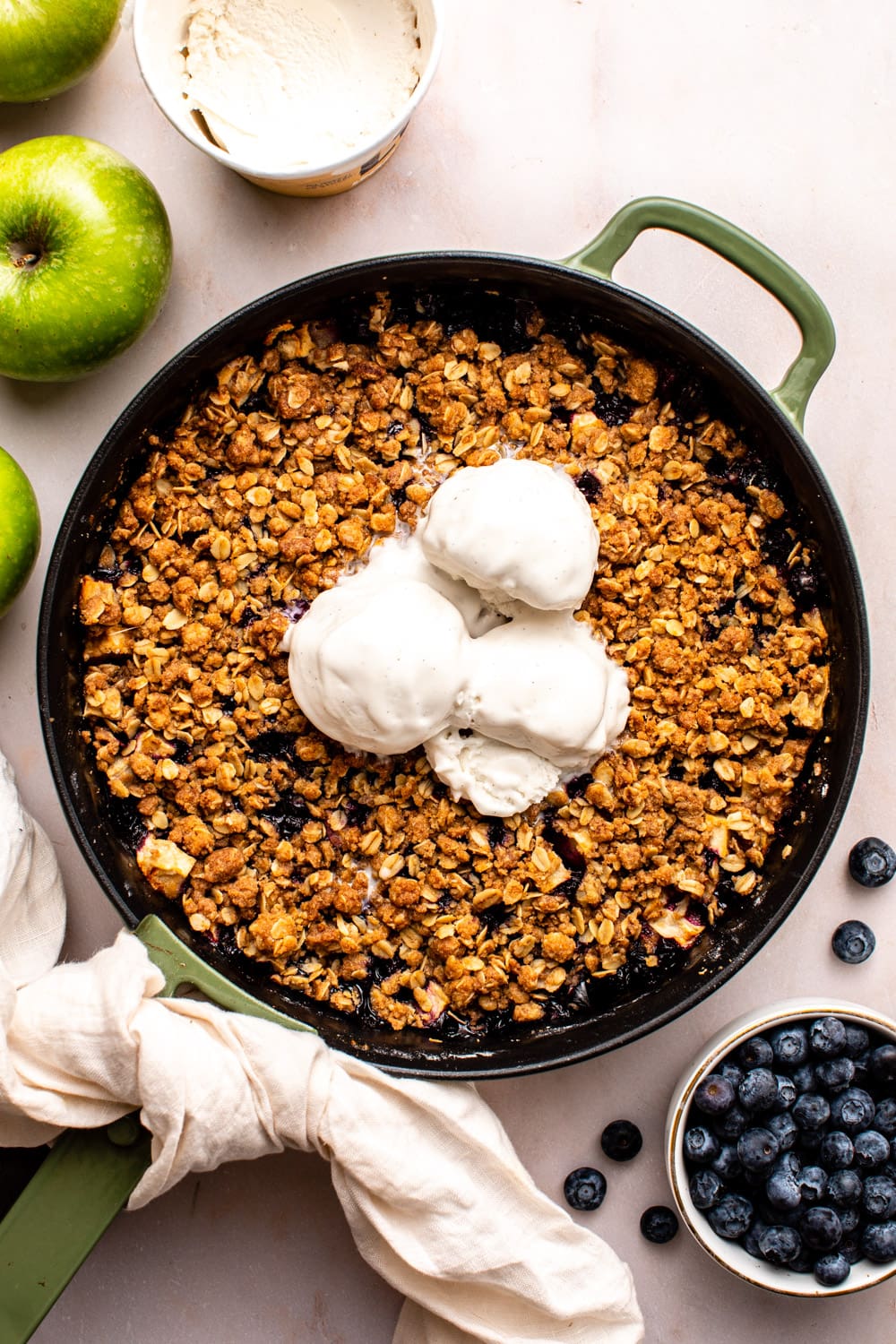 apple blueberry crisp in a pan served with three scoops of vanilla ice cream on top