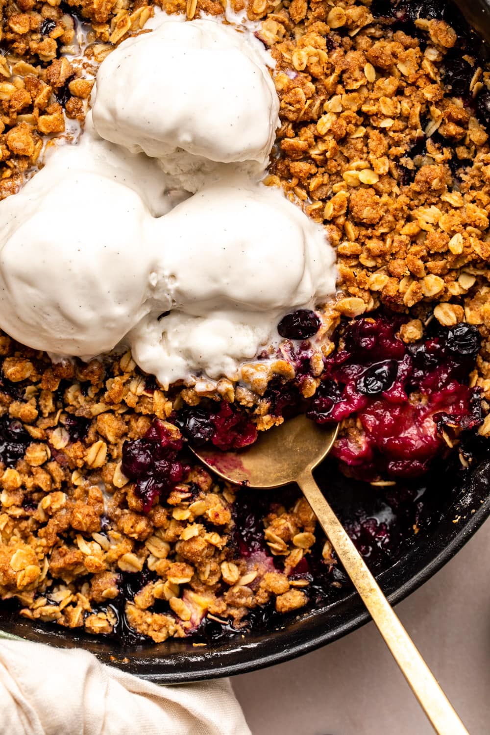a zoomed in image of apple blueberry crisp served with vanilla ice cream on top with a spoon digging up a portion