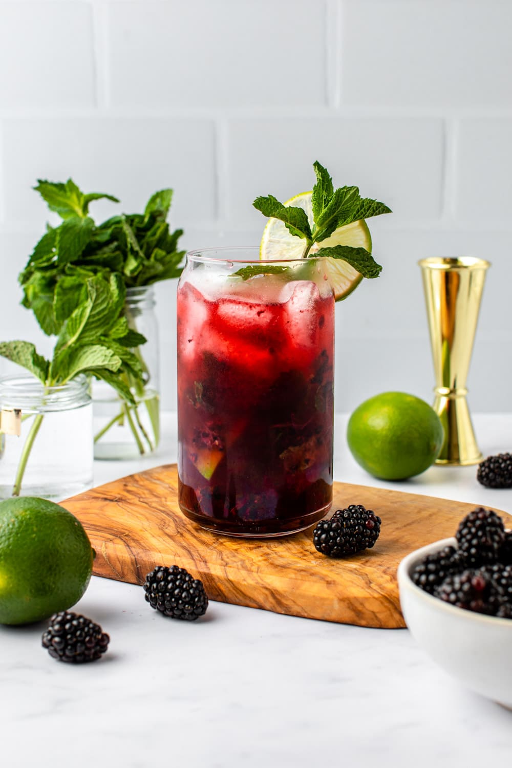 blackberry mojito served in a glass cup on a cutting board with berries, lime and fresh mint used as decoration