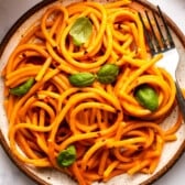 Roasted red pepper pasta swirled on plate and topped with fresh basil