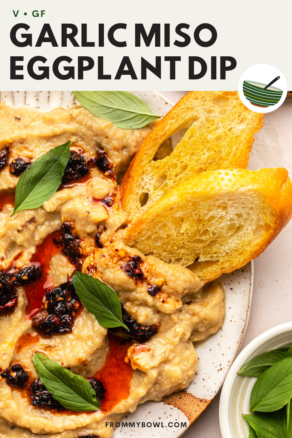 garlic miso eggplant dip served on a white plate and topped with thai basil, chili crisp and toasted bread