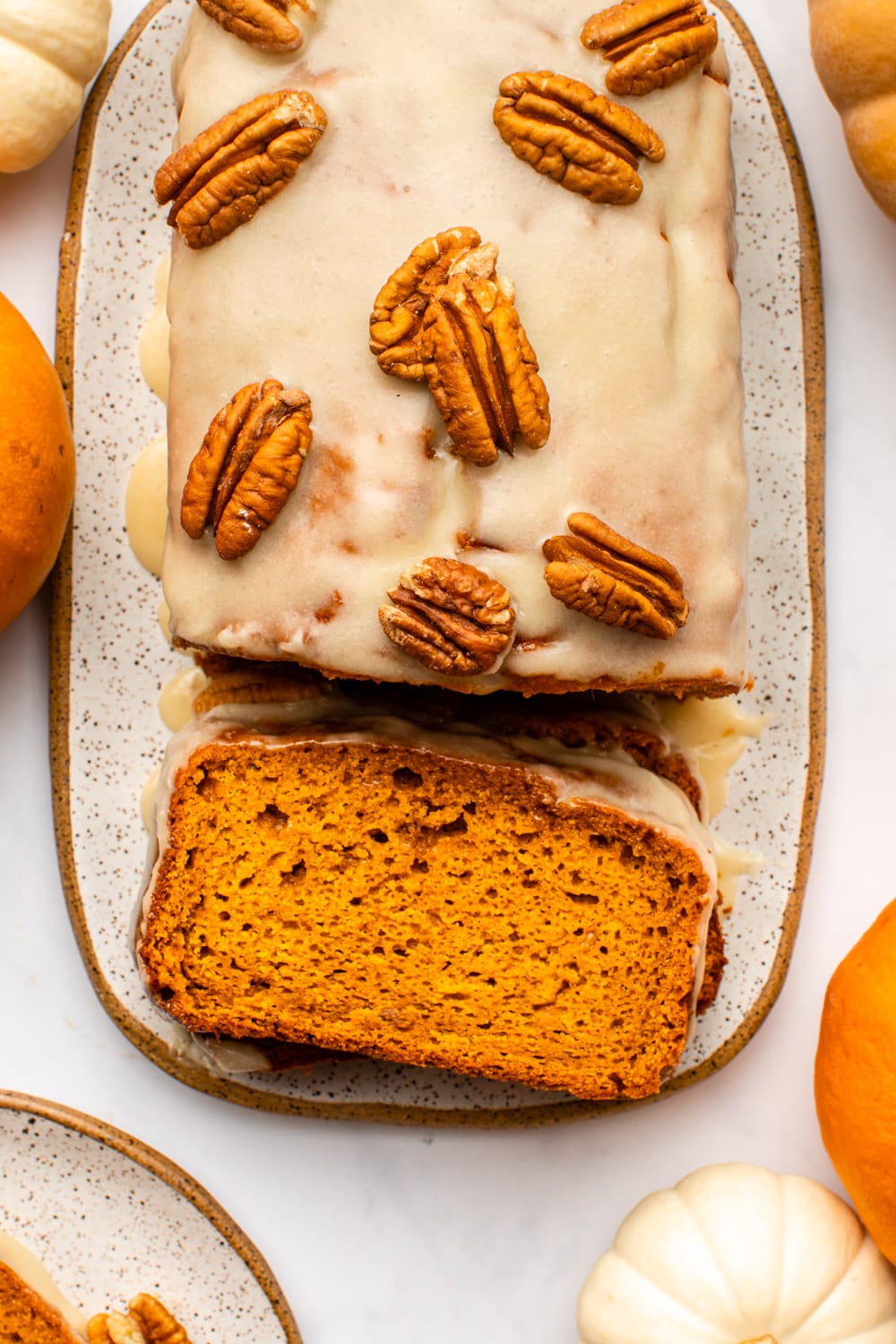 vegan pumpkin bread served with a glaze and topped with walnuts on a wide plate with several slices stacked on top