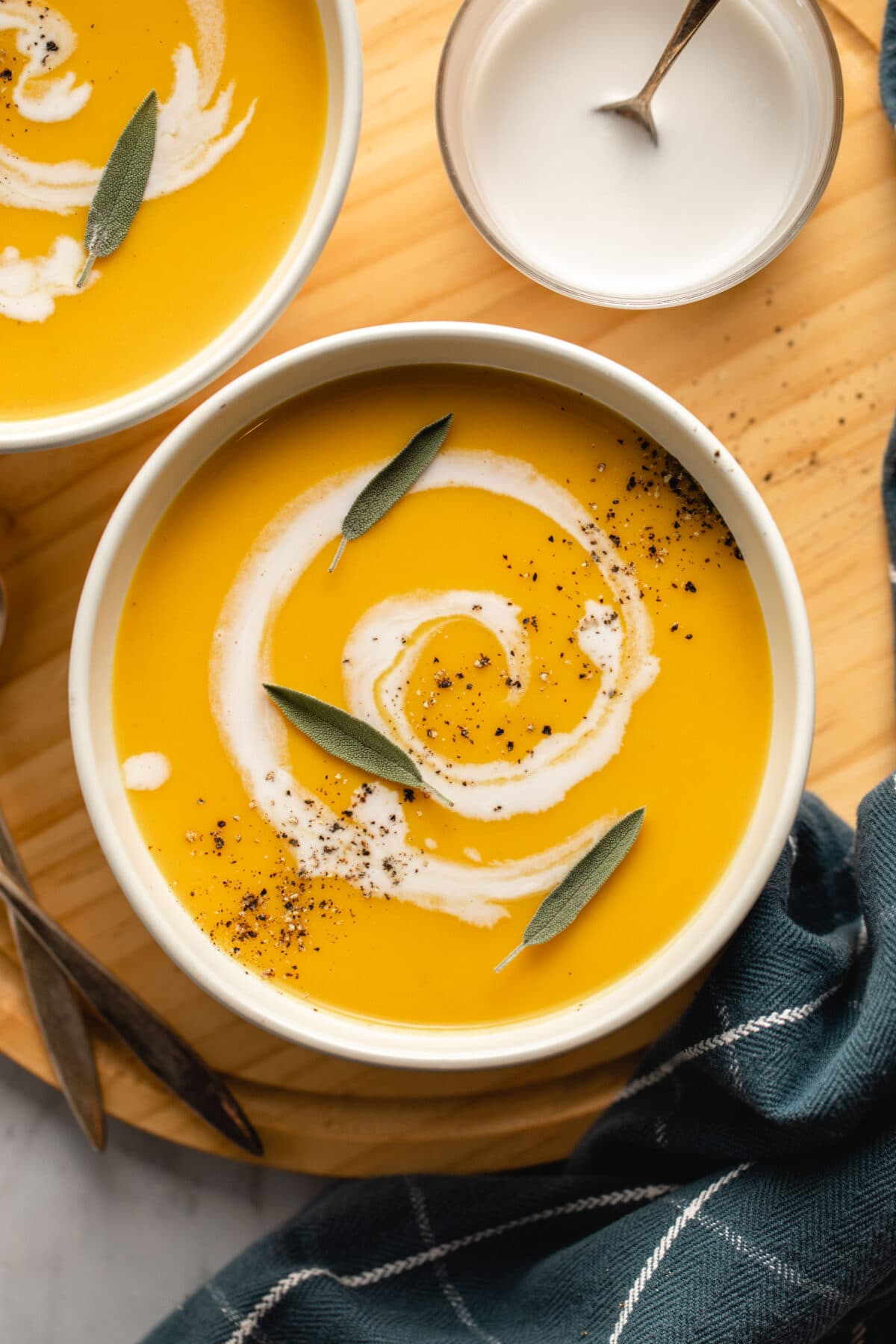 two bowls of butternut squash and apple soup in white bowl on wooden cutting board with marble background