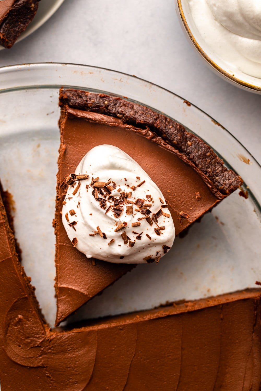 a zoomed in image of a slice of vegan chocolate pie in a pan, topped with coconut cream and chocolate flakes