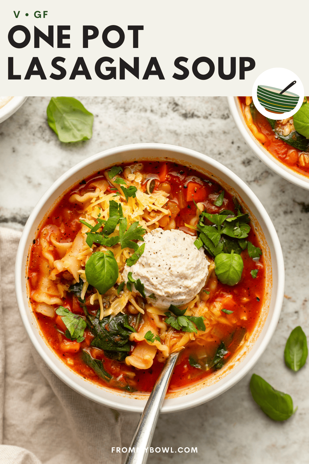 Close-up photo of vegan lasagna soup topped with ricotta cheese, and fresh herbs on stone countertop