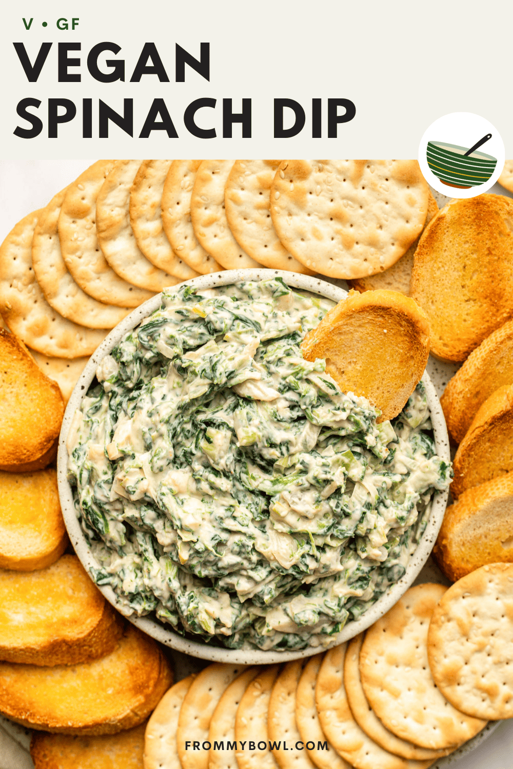 vegan spinach dip served in a white bowl with crackers and toasted crostini, with a single crostini dug in the spinach dip bowl
