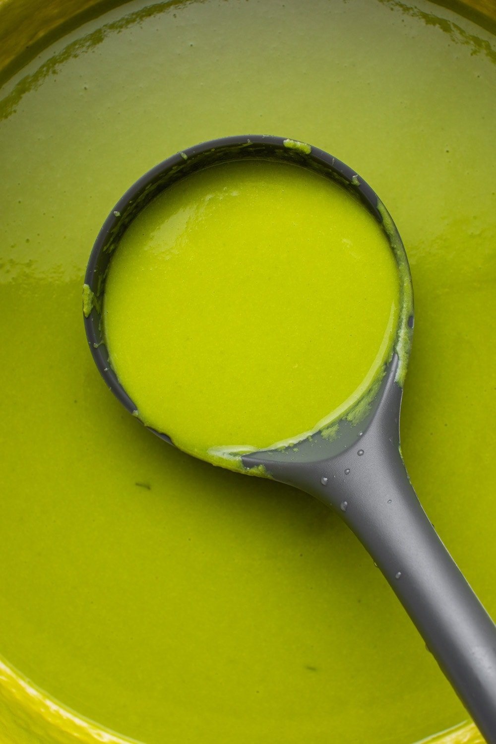 a zoomed in image of a serving spoon digging in on the green pea soup to show the soup's texture