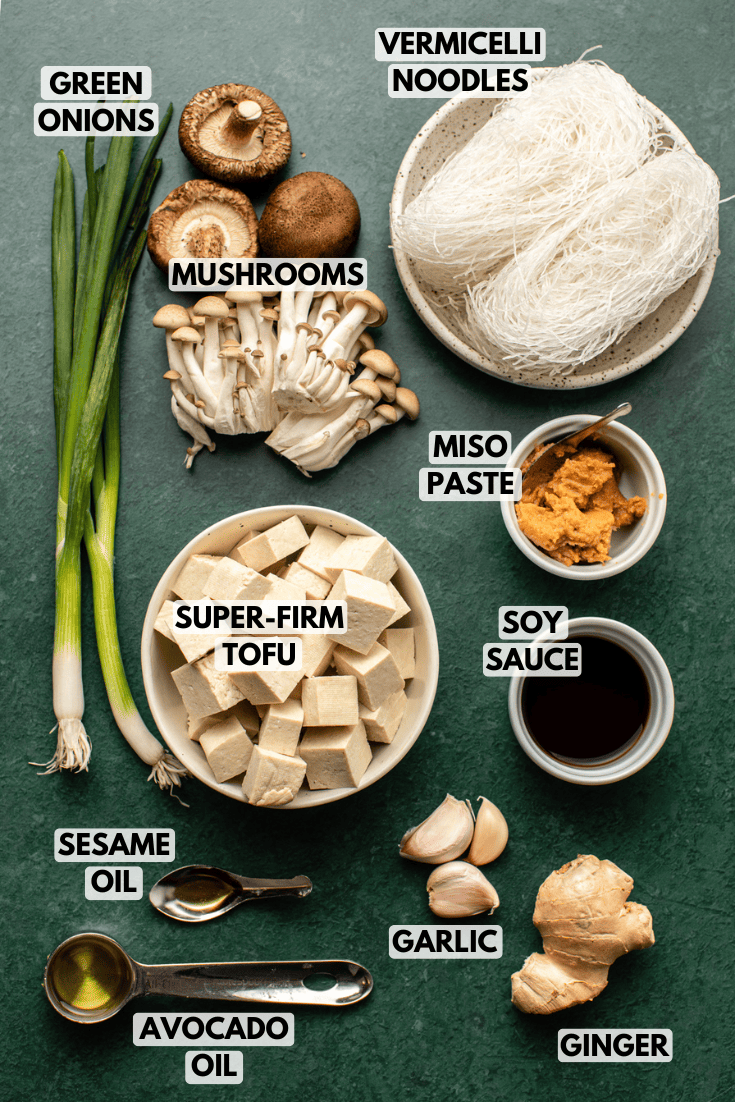ingredients for rice noodle soup arranged in various sizes of white bowls on a dark green kitchen countertop