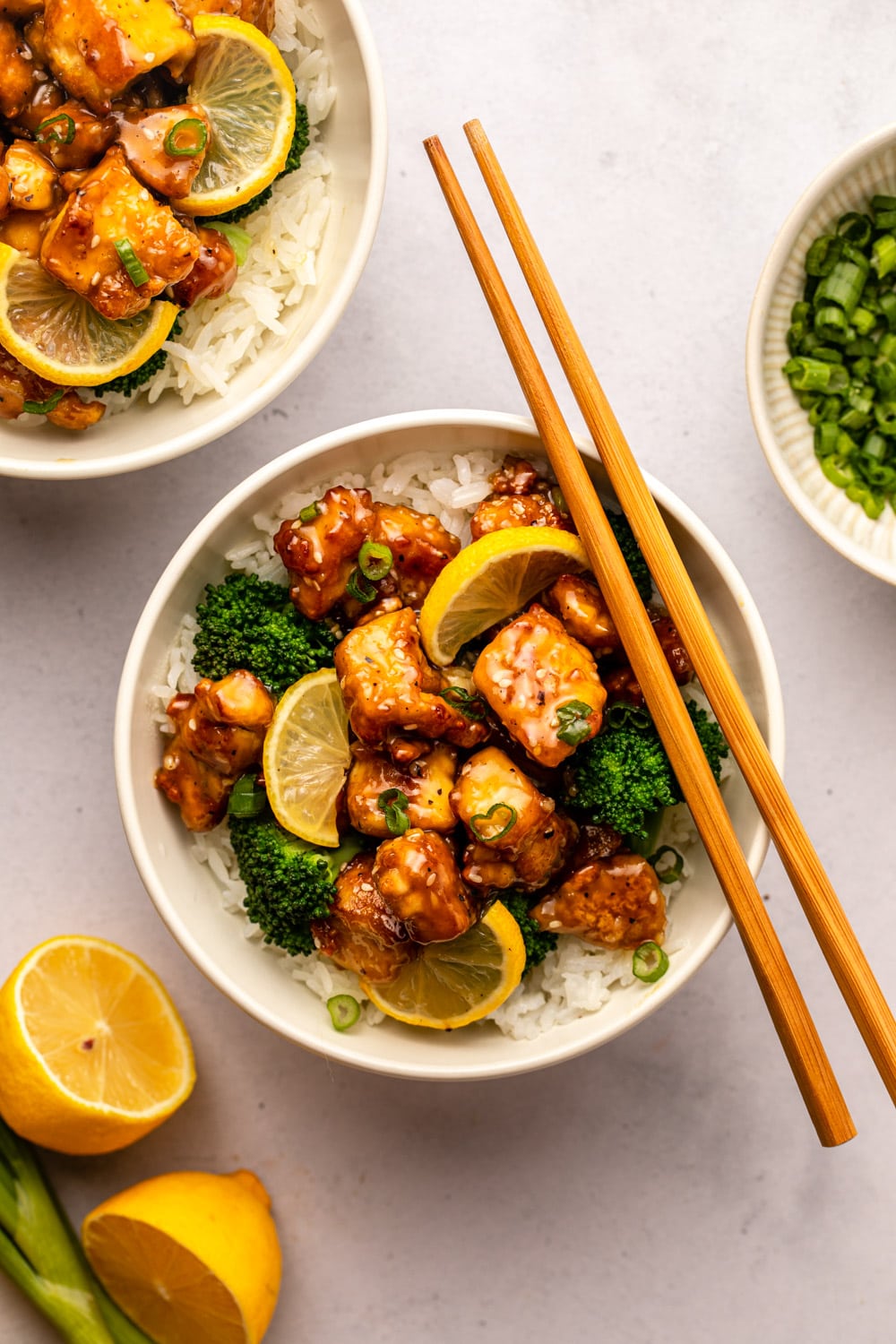 chinese lemon tofu served over rice with steamed broccoli in a white bowl, which chopsticks placed on top of the plate