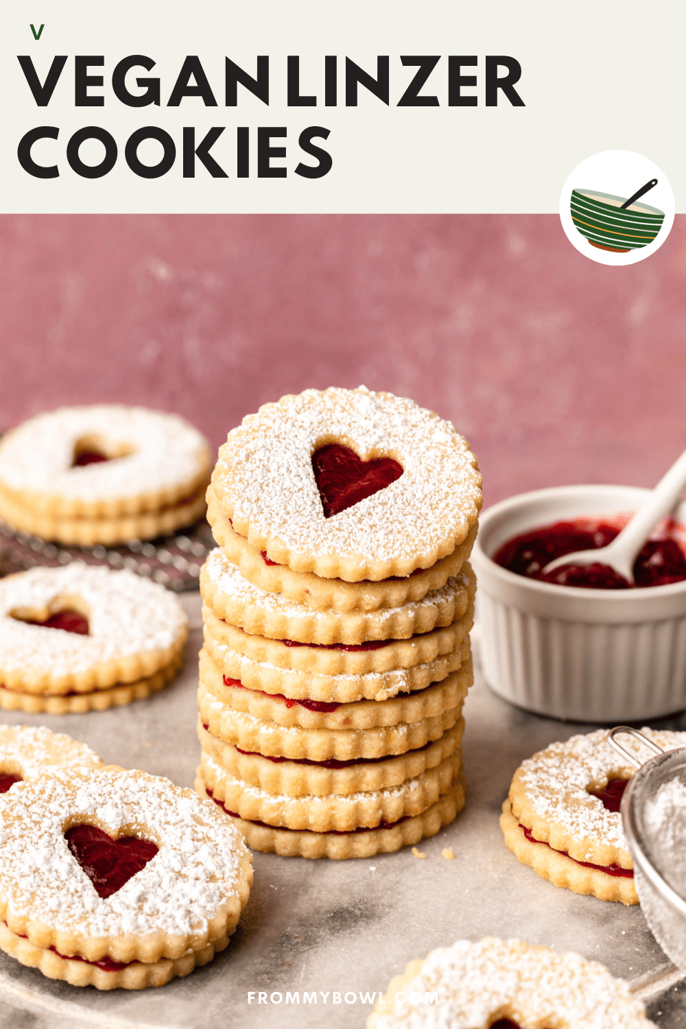 four vegan linzer cookies stacked on top of each other on a marble kitchen countertop with a burgundy backdrop, surrounded by five other cookies, a cooling rack, raspberry jam served in a small white bowl and powdered sugar in a sieve
