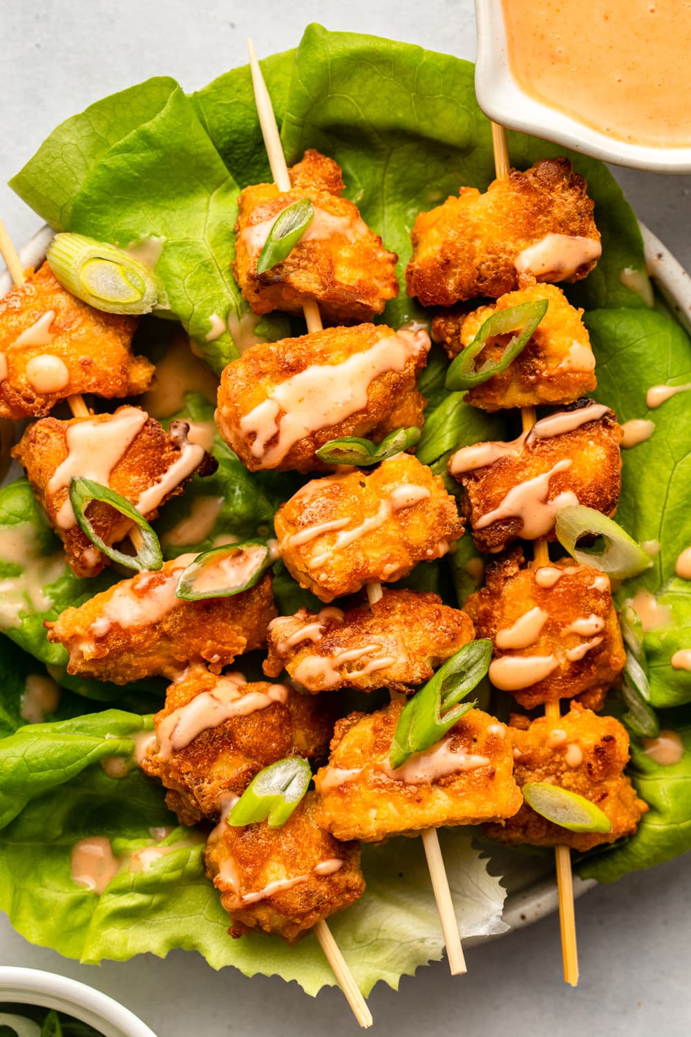 bang bang tofu in skewers served on lettuce and topped with bang bang sauce and green onions