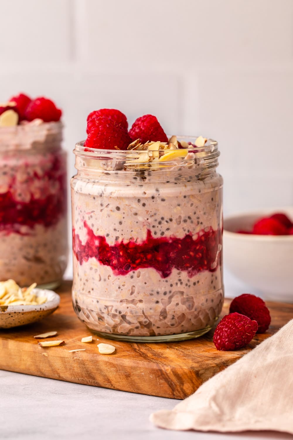 raspberry overnight oats served in a jar on a cutting board topped with fresh raspberries and silvered almonds