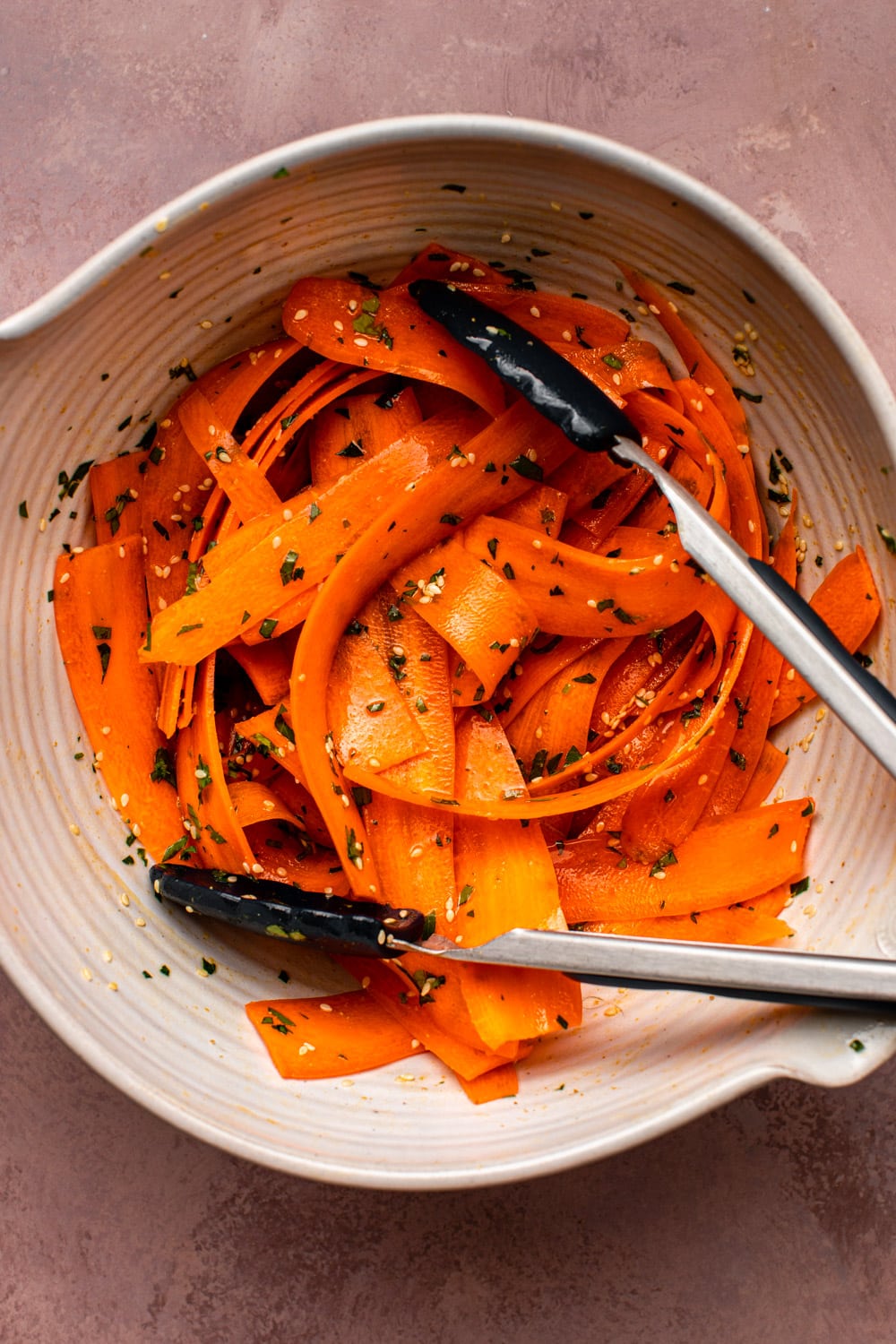 raw carrot salad served on a wide bowl with a pair of tongs tossing the salad