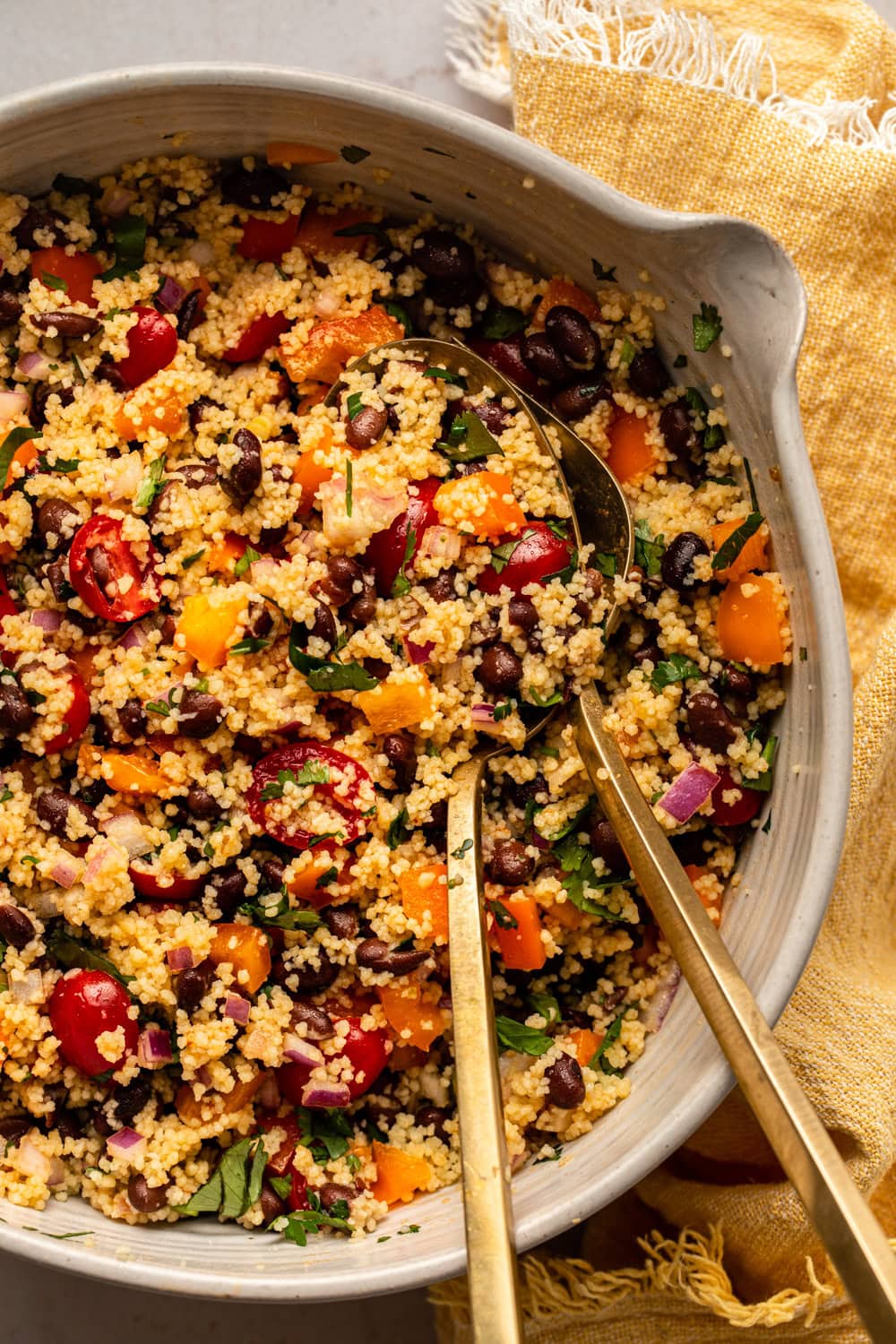 black bean couscous salad in a large bowl with two spoons mixing the salad