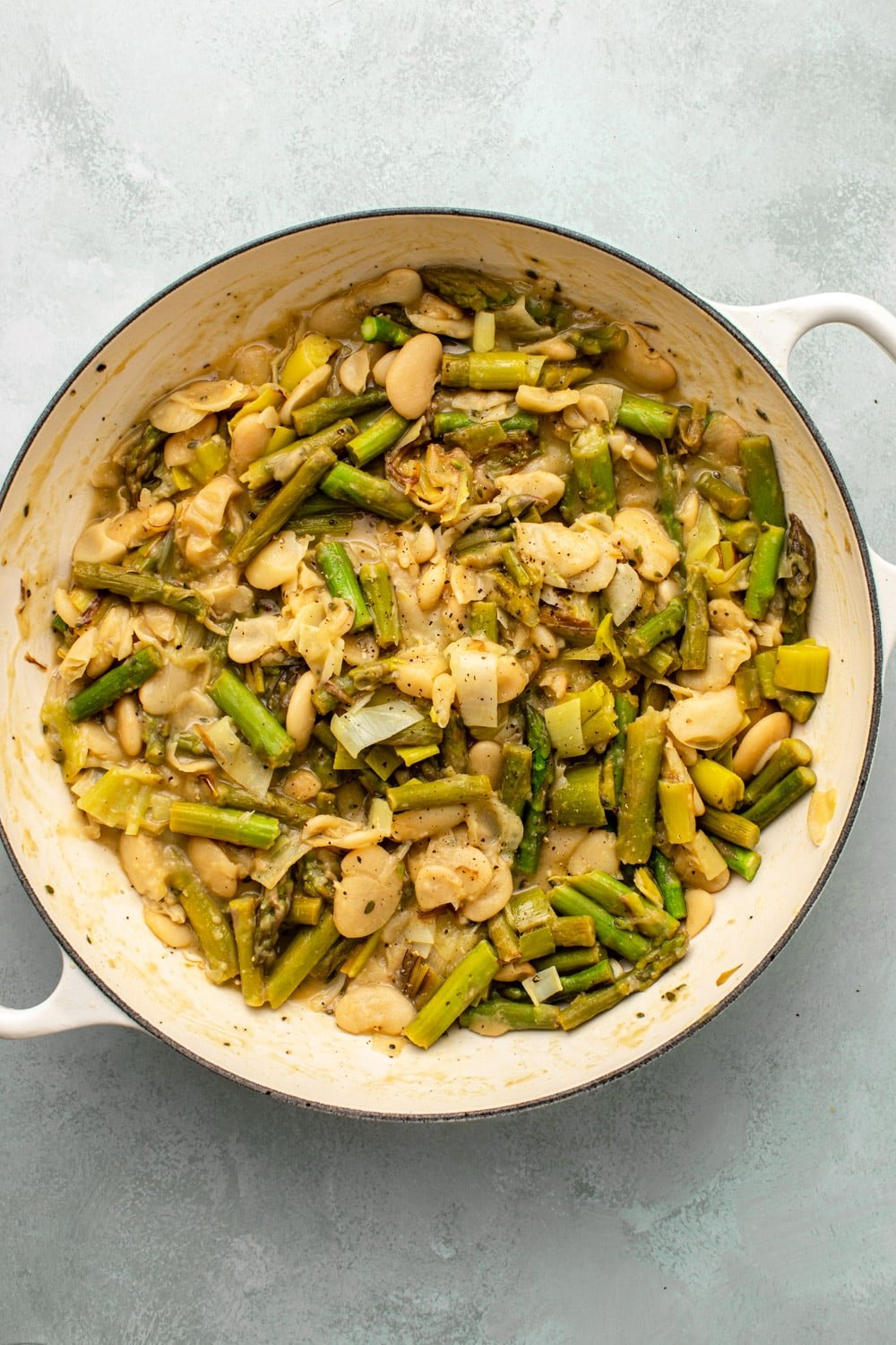 a photo of the pan with the cooked braised asparagus and butter beans placed on a light green kitchen countertop