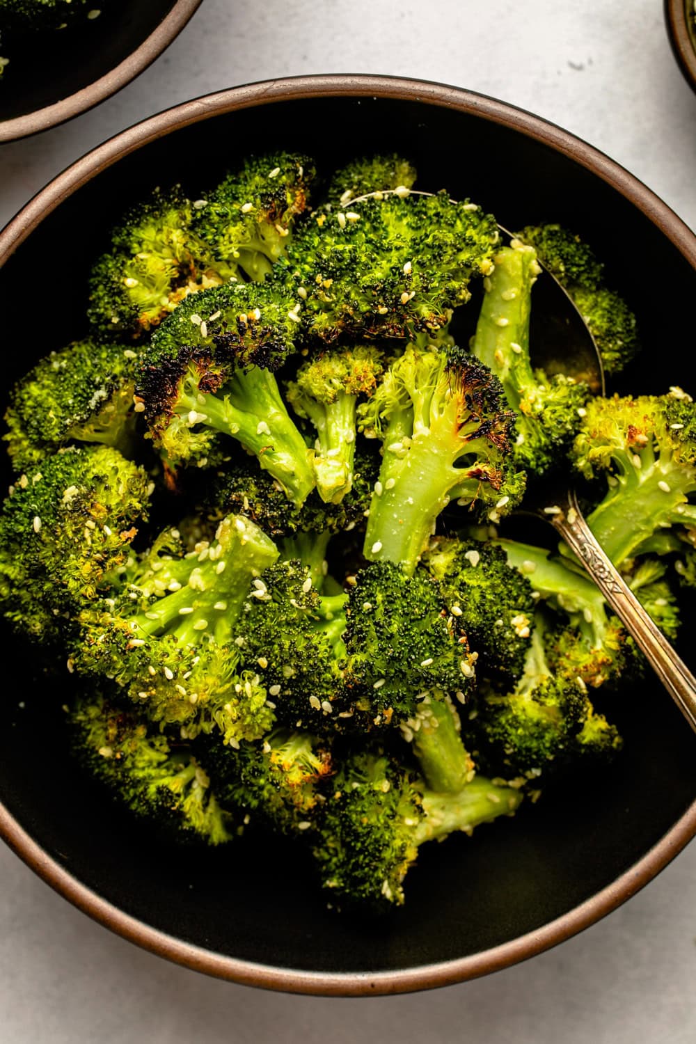 roasted garlic sesame broccoli served in a black bowl with a metal spoon scooping up several broccoli