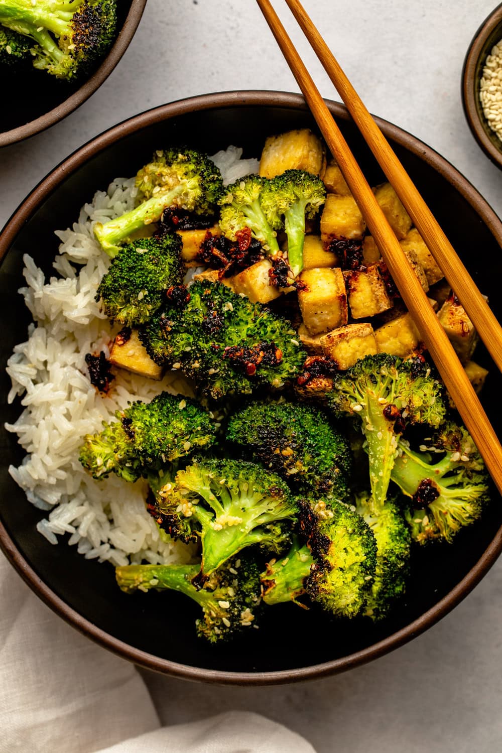 roasted garlic sesame broccoli served with rofu and rice with chopsticks placed on a black bowl