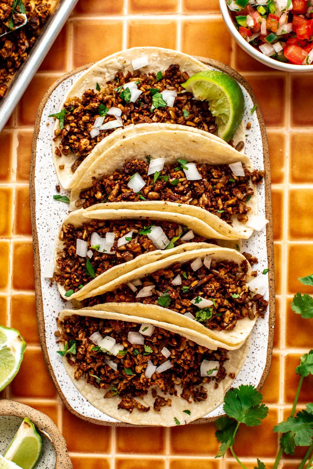 five tacos made with sheet pan vegan taco meat served on an oval plate and topped with a slice of lime