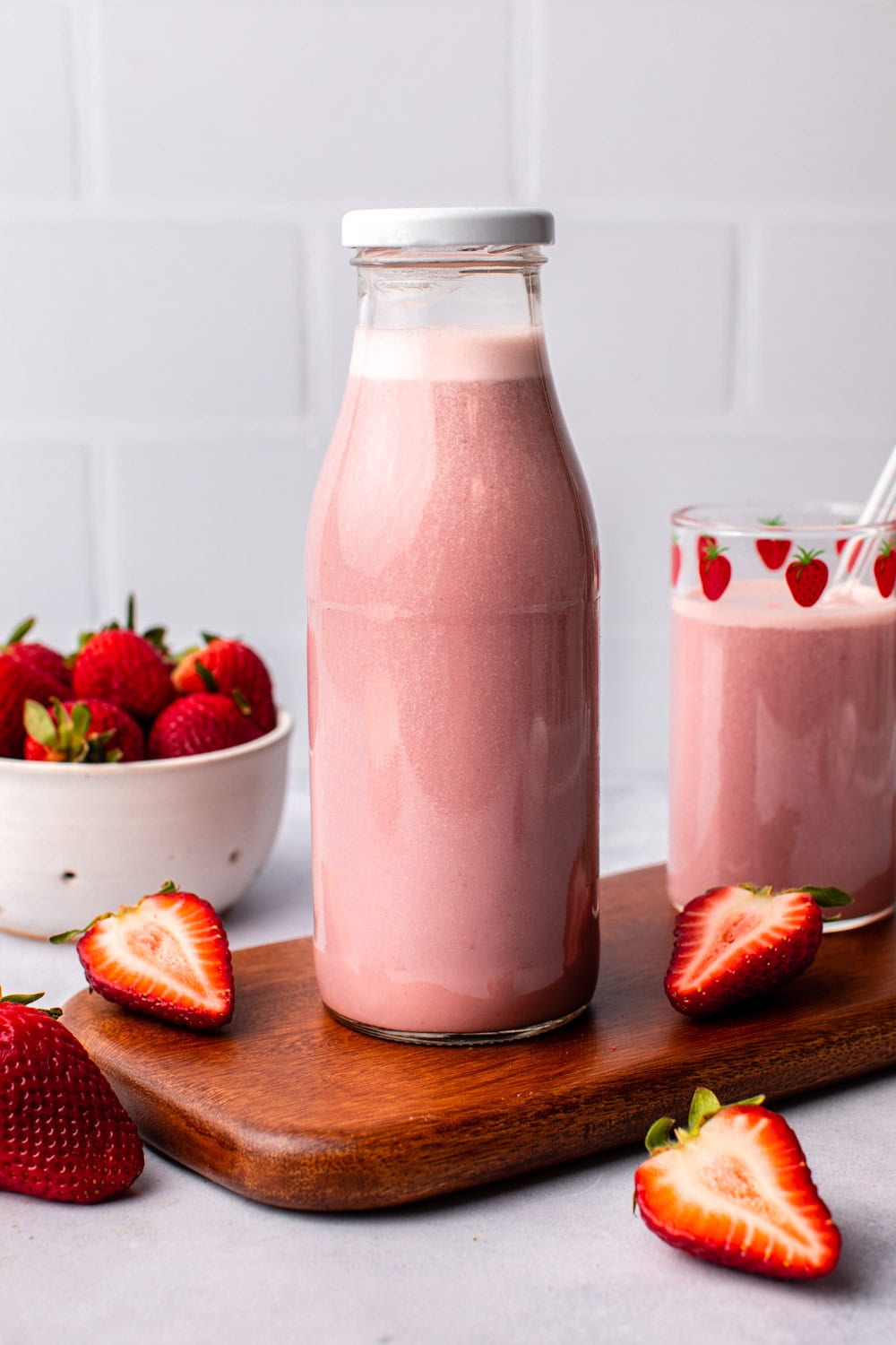 vegan strawberry milk served in a glass bottle on a cutting board surrounded by strawberry pieces