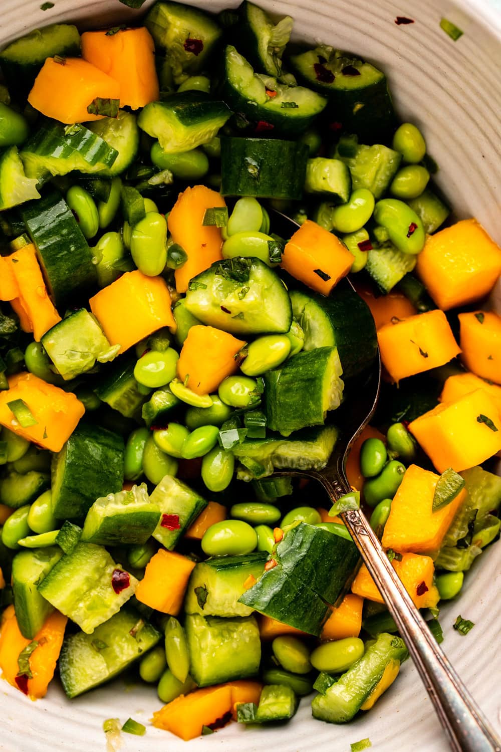 a zoomed in image of mango cucumber salad in a huge bowl with a spoon digging up a bite to show the texture of the salad