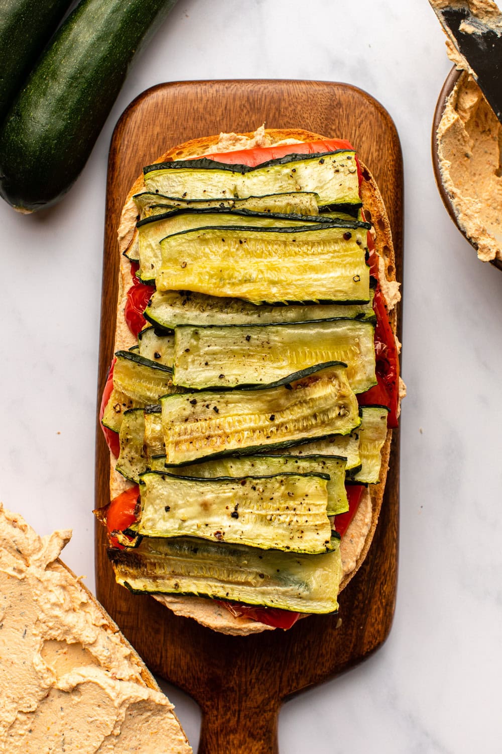 open-faced roasted zucchini sandwich placed on a cutting board on a marble kitchen countertop