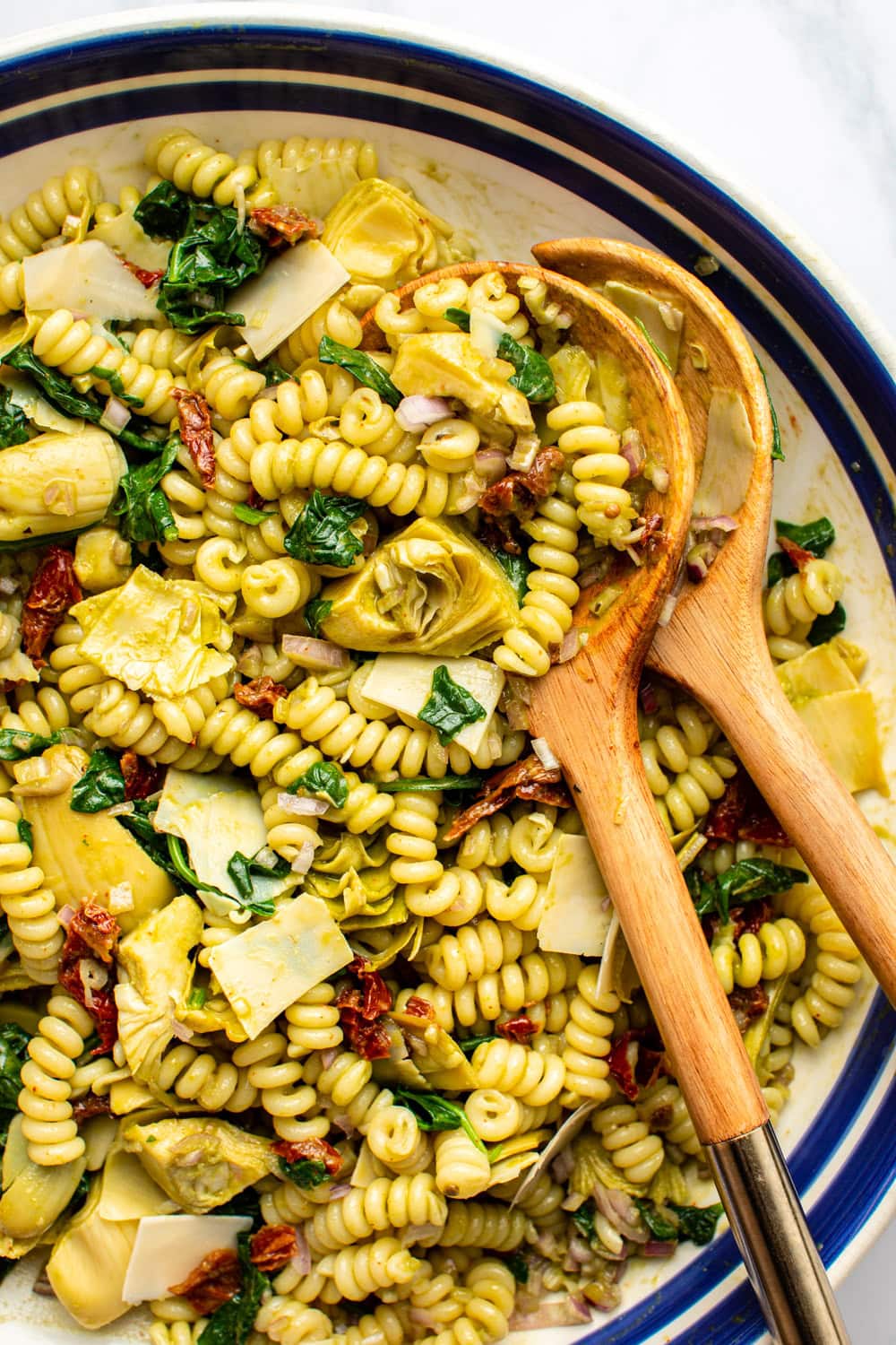 spinach artichoke basil pasta served in a wide bowl with two wooden spoons dug in