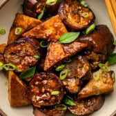 sticky eggplant and tofu in tan serving bowl topped with green onions and thai basil