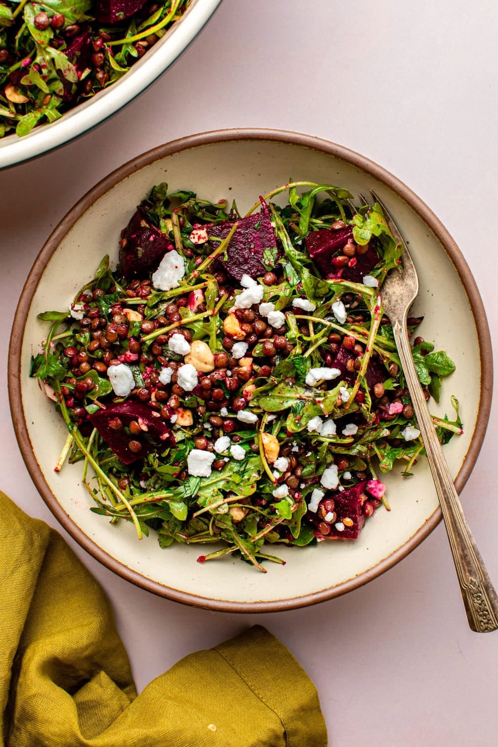 beet and lentil salad in a white ceramic bowl on a kitchen countertop, with a fork resting in the bowl and a green kitchen towel visible in the frame