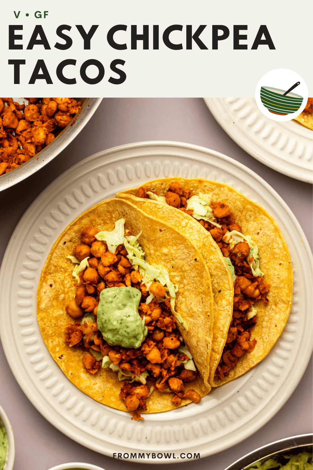 chickpea tacos served on a ceramic plate, with a small bowl of lime wedges, a side of avocado crema, and a baking tray visible in the background