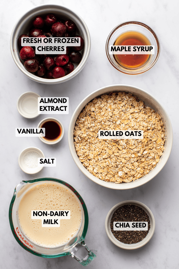 ingredients for cherry overnight oats arranged in bowls, including oats, cherries, chia seeds, plant milk, and maple syrup.