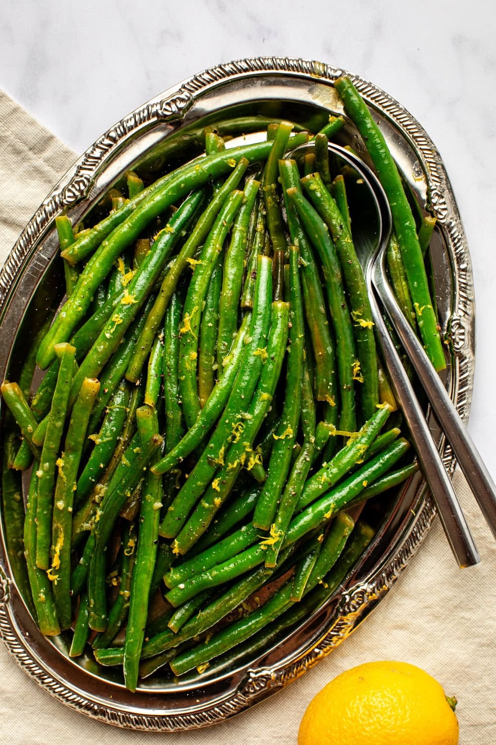 freshly cooked lemon green beans served on a silver platter with serving utensils.