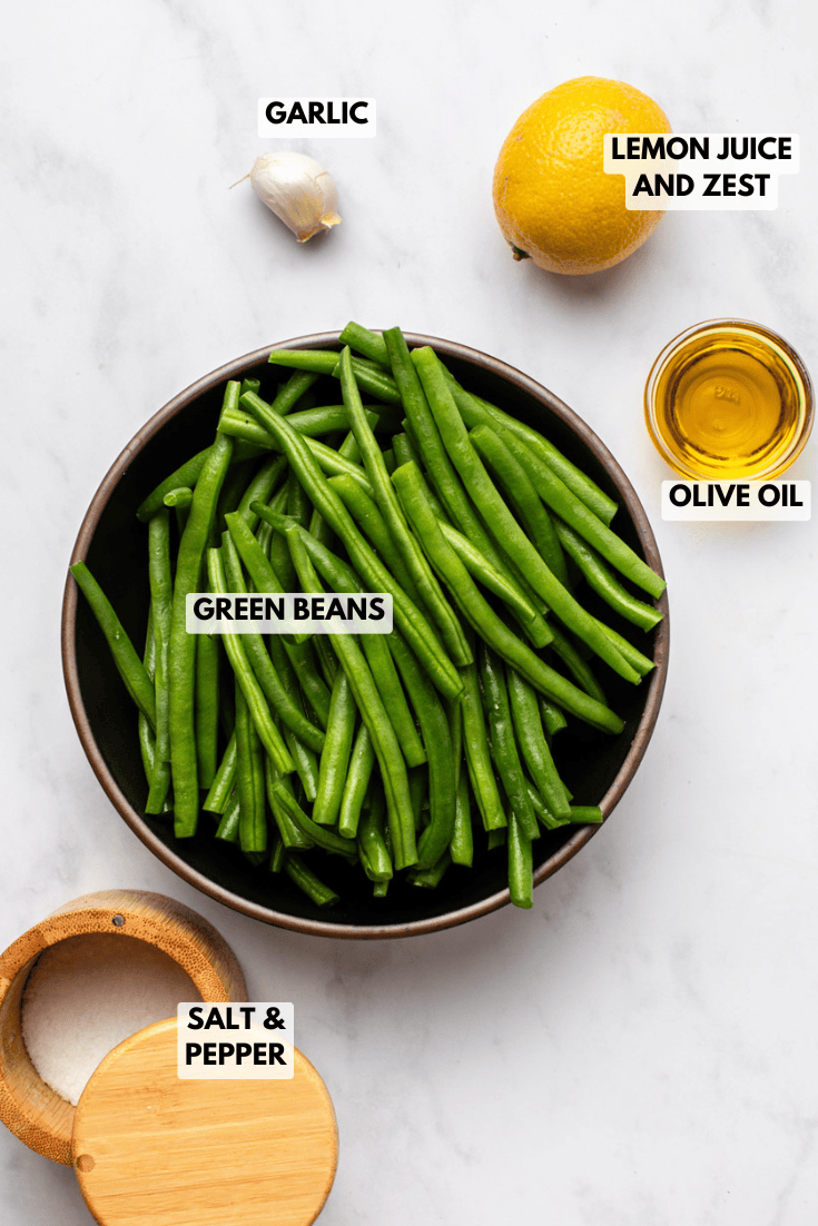 ingredients for lemon green beans arranged on a white surface: fresh green beans, garlic, lemon, olive oil, salt, and black pepper.
