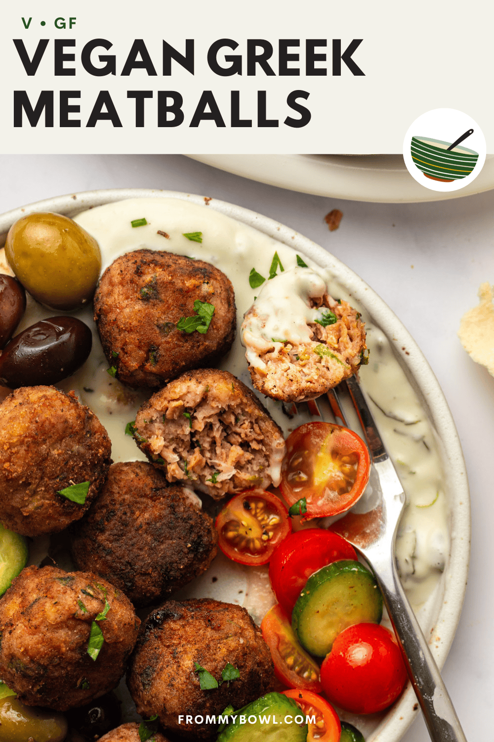a white ceramic plate on a kitchen countertop topped with pita bread, vegan greek meatballs, tomatoes, cucumber, olives, and tzatziki. a fork rests on the plate, and one of the meatballs has been cut in half to reveal its texture.