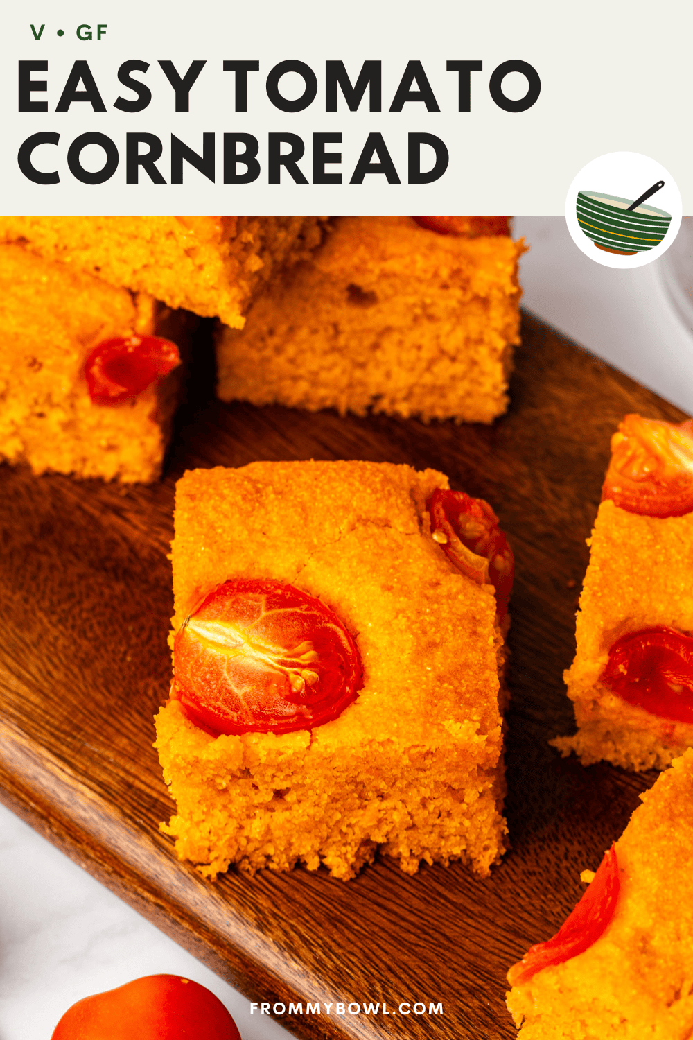tomato cornbread cut into squares and topped with roasted cherry tomatoes, served on a wooden board.