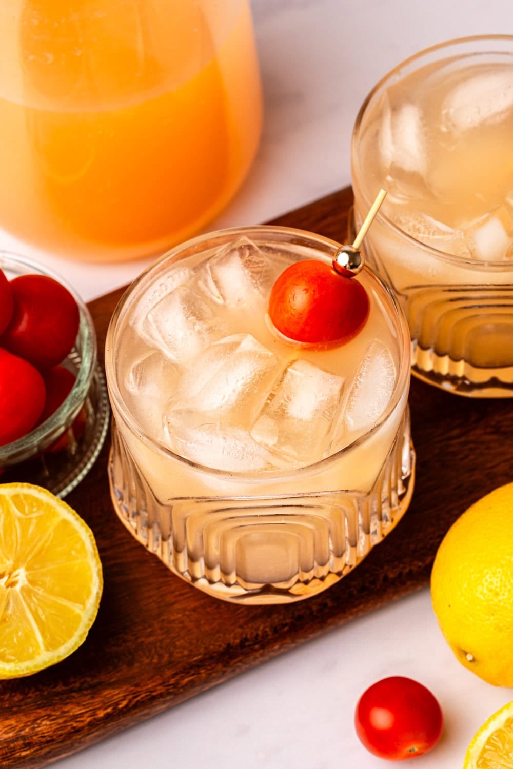 two glasses of sparkling tomato lemonade on a wood cutting board, garnished with cherry tomatoes