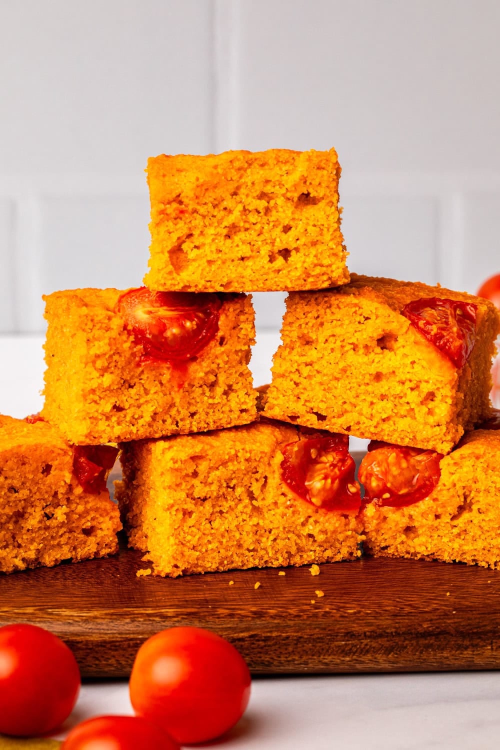 thick slices of golden tomato cornbread stacked on a wooden board, with roasted cherry tomatoes baked into the top.