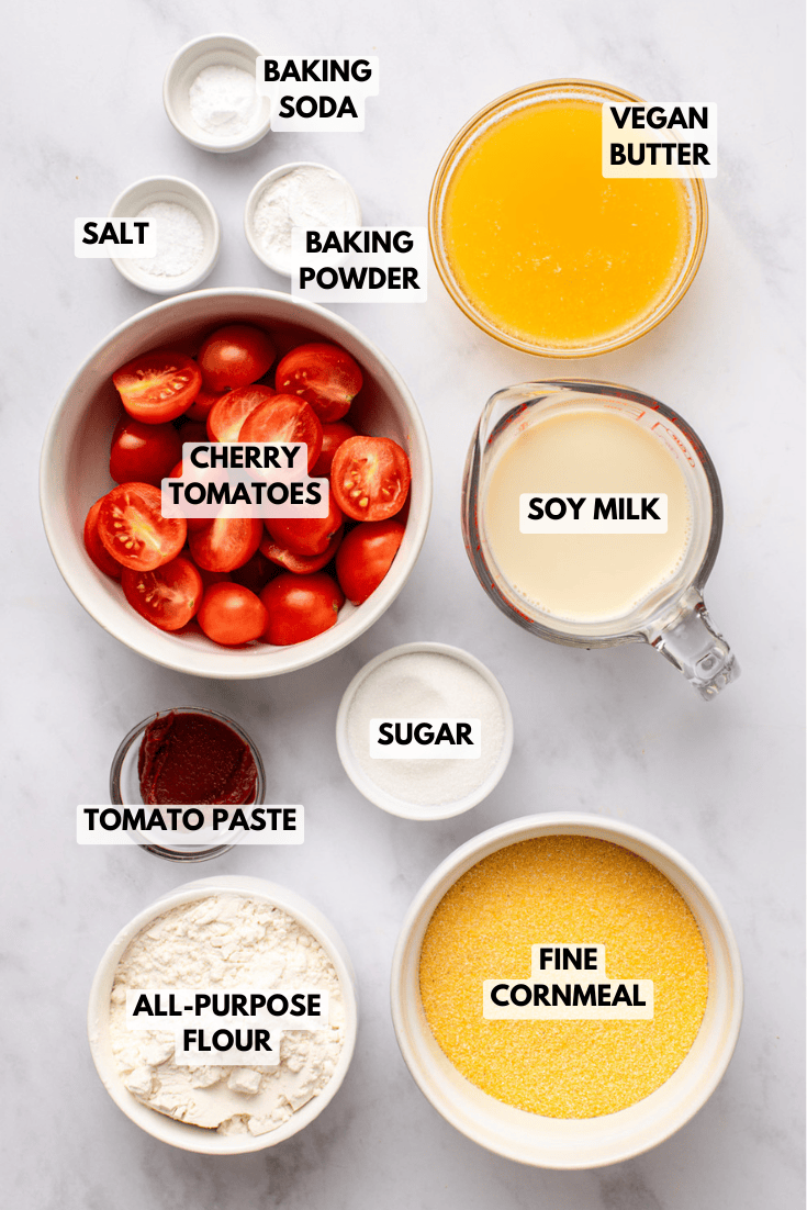 ingredients for vegan tomato cornbread, including cornmeal, flour, cherry tomatoes, tomato paste, soy milk, vegan butter, sugar, and leavening agents.
