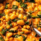 silver serving spoon scooping cooked gnocchi and chickpeas out of dish